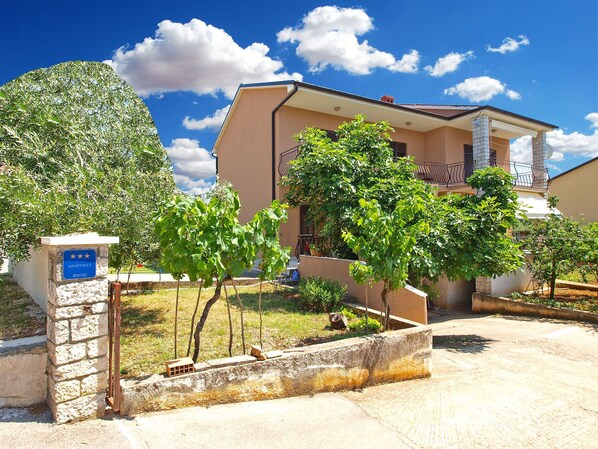 A residential building with a stone entrance, a balcony, and a garden with trees.