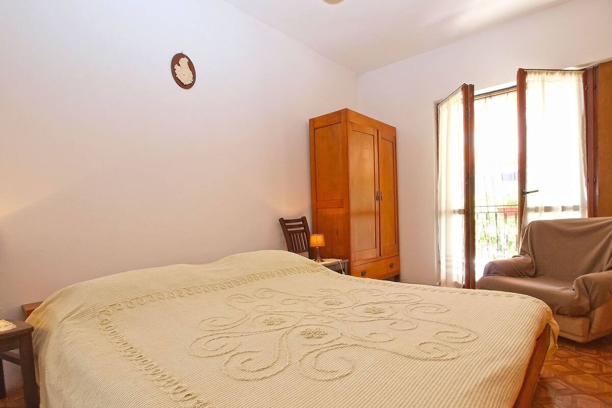 Une chambre avec un grand lit, une armoire en bois, une chaise et une fenêtre avec des rideaux.