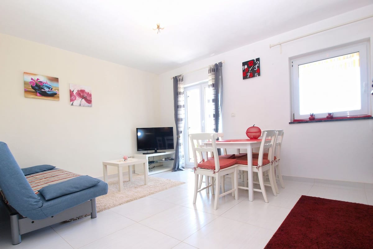 A living room with a sofa, a TV, a dining table with chairs, and artwork on the walls.