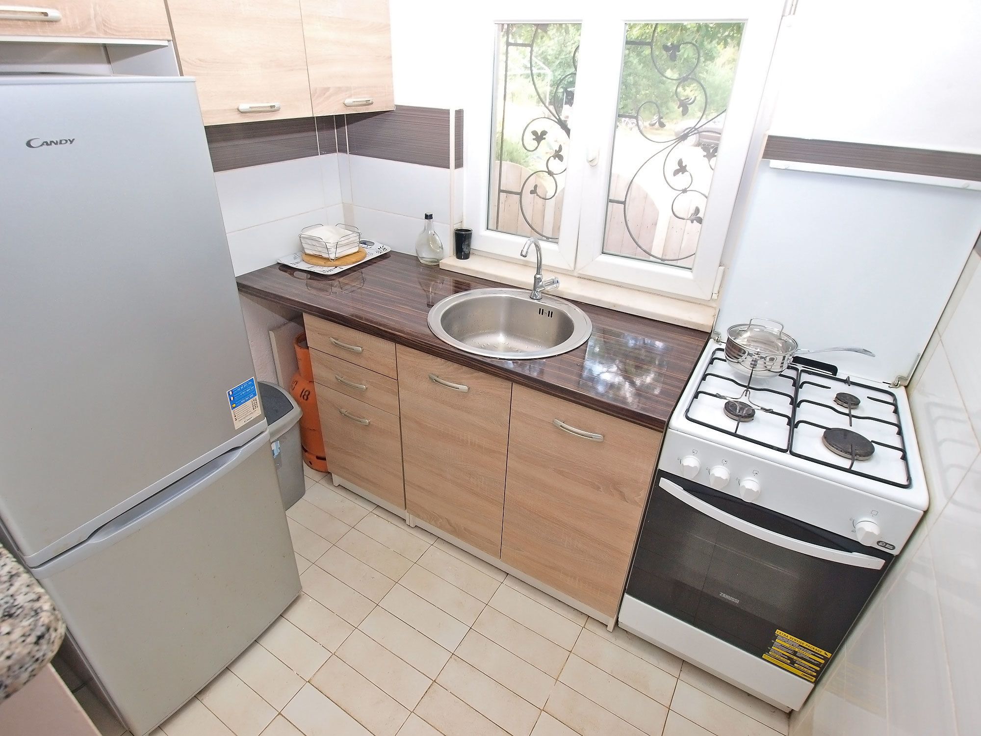 Una cocina compacta con refrigerador, pileta, estufa y alacenas de madera.
