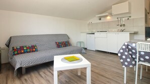 Ett kompakt bostadsutrymme med en soffa, ett litet bord, en köksdel och ett matbord.