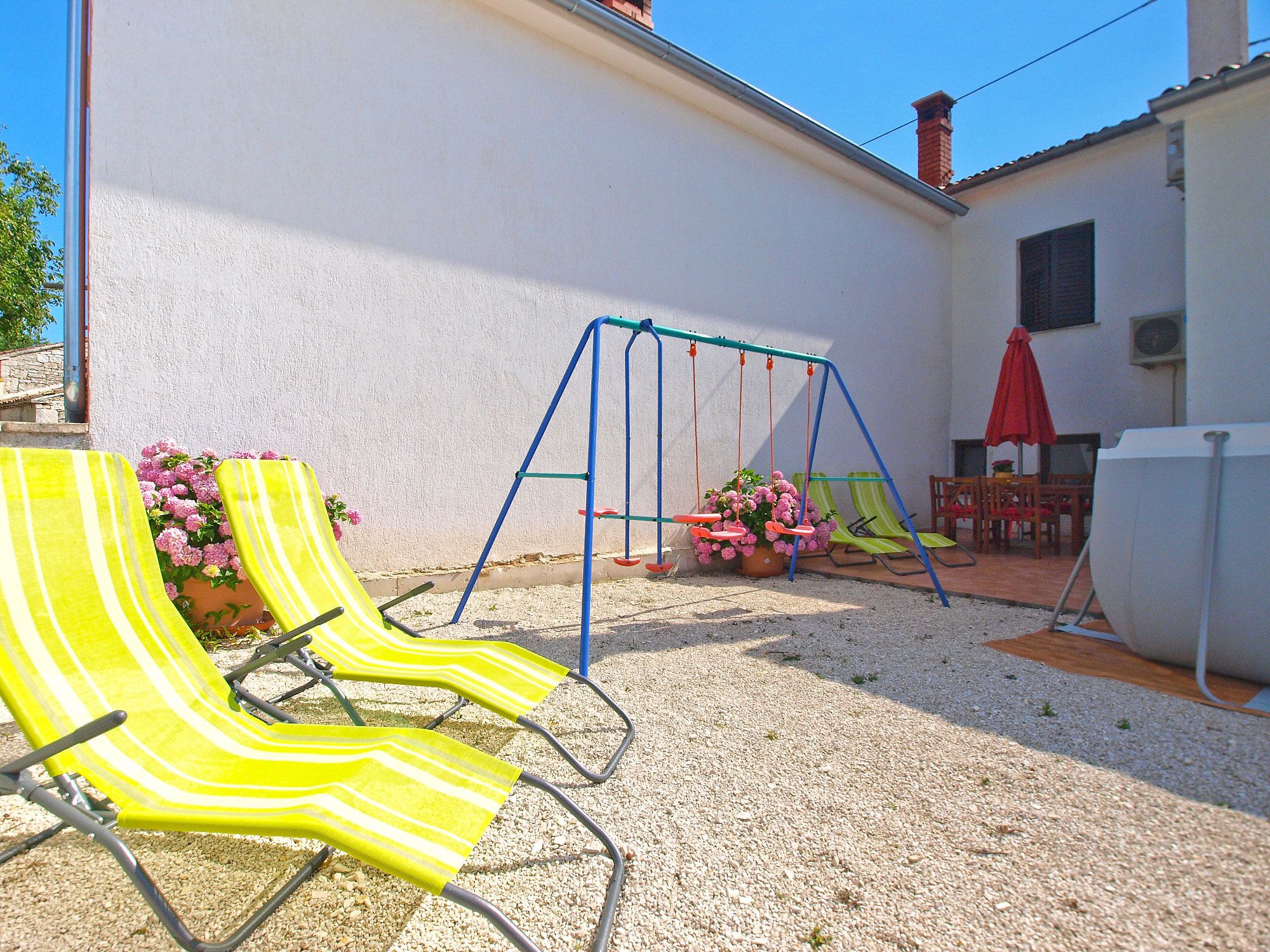 A patio with two yellow striped lounge chairs, a swing set, and a red umbrella.