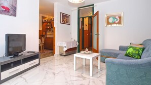 A living room with a TV, a small table, a sofa, and a door leading to a kitchen. - Apartment 1431 (Pula)