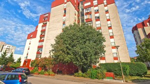 A multi-story residential building with a red and beige facade, large windows, and a tree in front. - Apartment 1431 (Pula)
