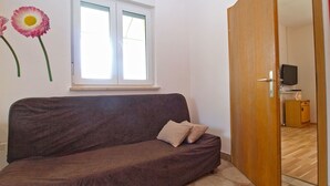 Una habitación con un sofá marrón, una ventana con persianas, una puerta de madera y un mueble bajo con un televisor.