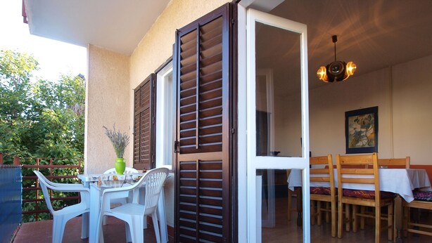 Une terrasse extérieure avec une table et des chaises, une porte-fenêtre coulissante et un luminaire fixé au plafond.