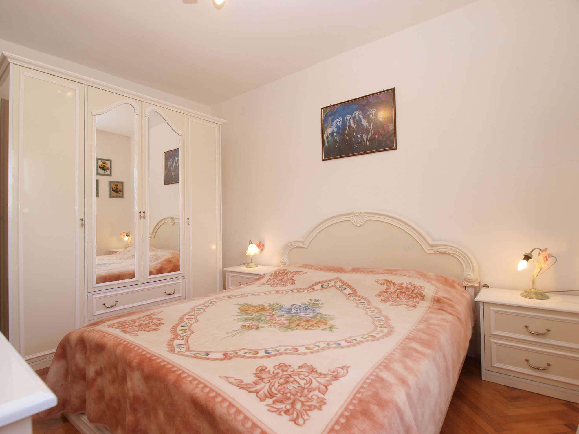 Een slaapkamer met een bed, nachtkastjes, een kledingkast en een schilderij aan de muur.