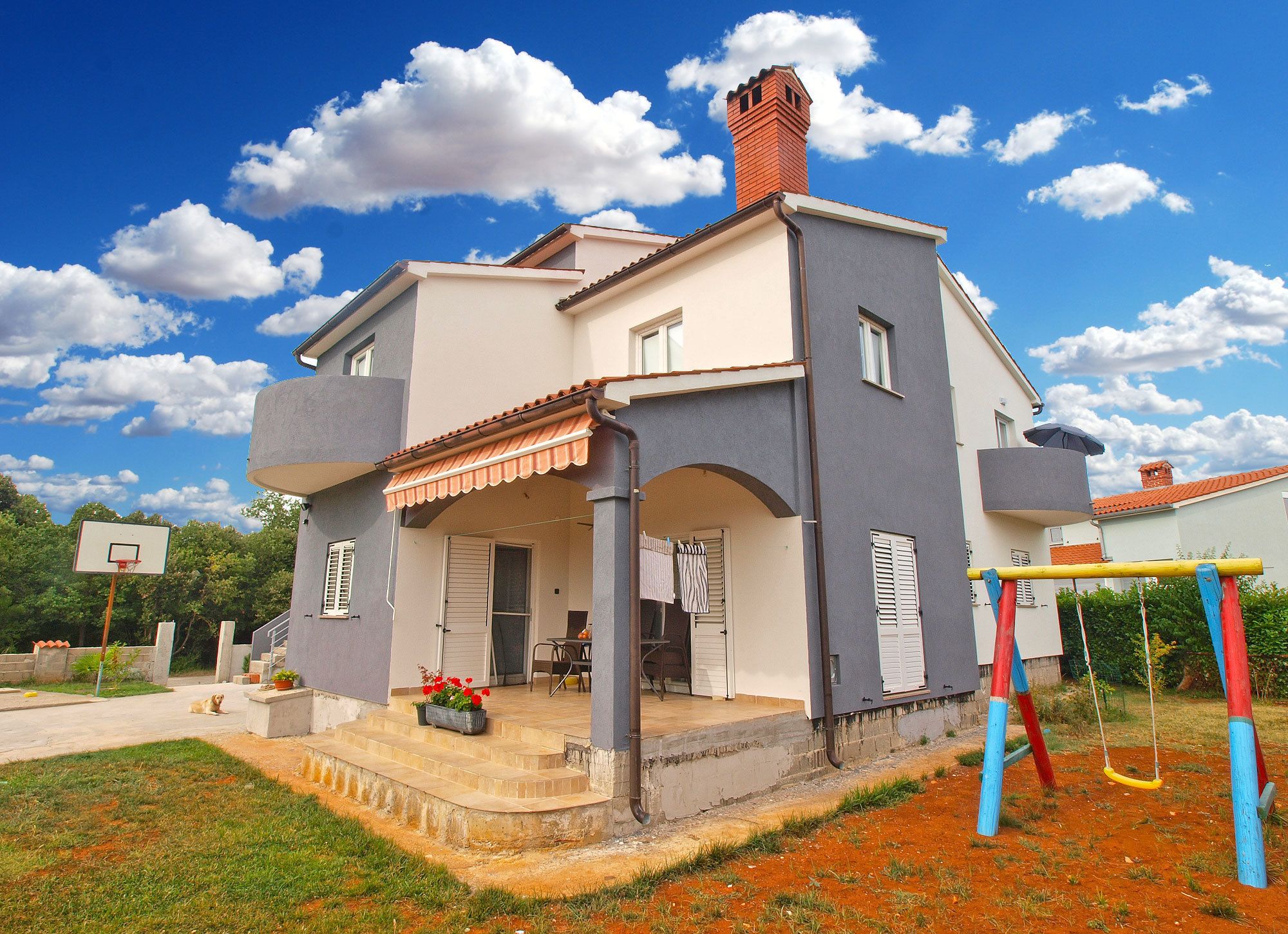 A two-story house with a balcony, a chimney, and a basketball hoop in the yard.