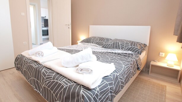 A neatly made bed with a patterned bedspread, a white headboard, and a bedside lamp. - Apartment 1449 (Pula)
