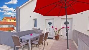 A terrace with a table and chairs, a red umbrella, and a potted plant with pink flowers. - Apartment 1449 (Pula)