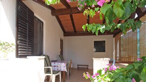 Een terras met een tafel en stoelen, een houten plafond en een bloempot met roze bloemen.
