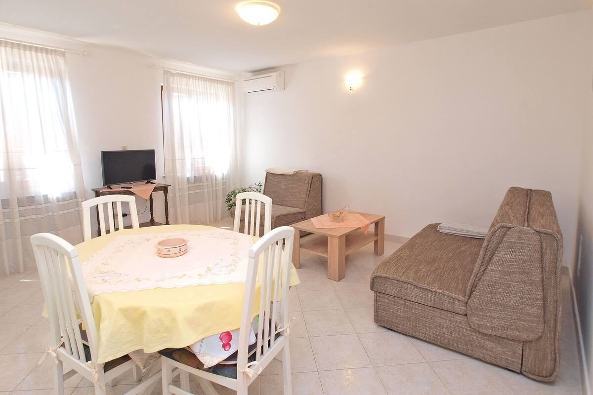 Una sala de estar con una mesa de comedor, sillas, un sofá, un televisor y un equipo de aire acondicionado.