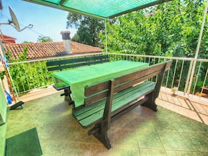 A covered outdoor area with a wooden bench and a table covered with a green tablecloth. - Apartment 1457 (Rovinj)
