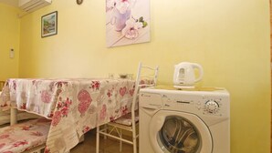 A laundry area with a washing machine, a table with floral tablecloths, and a painting of flowers on the wall. - Apartment 1462 (Pula)