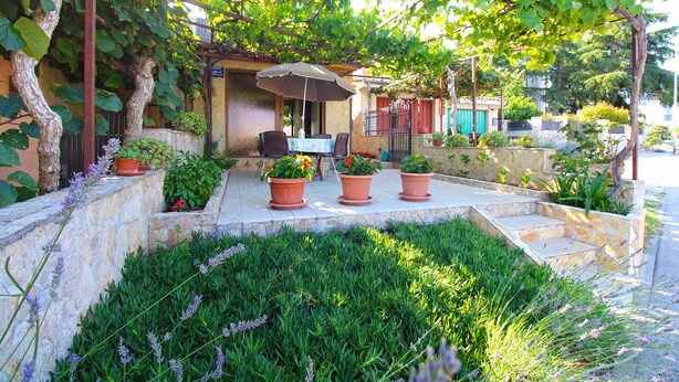 An outdoor seating area with a table and chairs under a pergola, surrounded by potted plants and a stone wall. - Apartment 1462 (Pula)