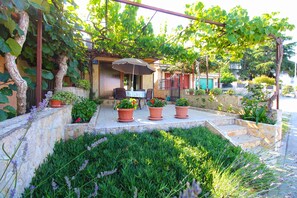 An outdoor seating area with a table and chairs under a pergola, surrounded by potted plants and a stone wall. - Apartment 1462 (Pula)