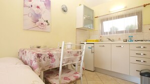 A compact kitchen with a dining area, featuring a small refrigerator, a sink, and a window with patterned curtains. - Apartment 1462 (Pula)