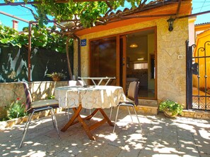 An outdoor patio with a table and chairs, a pergola with grapevines, and a stone wall. - Apartment 1462 (Pula)