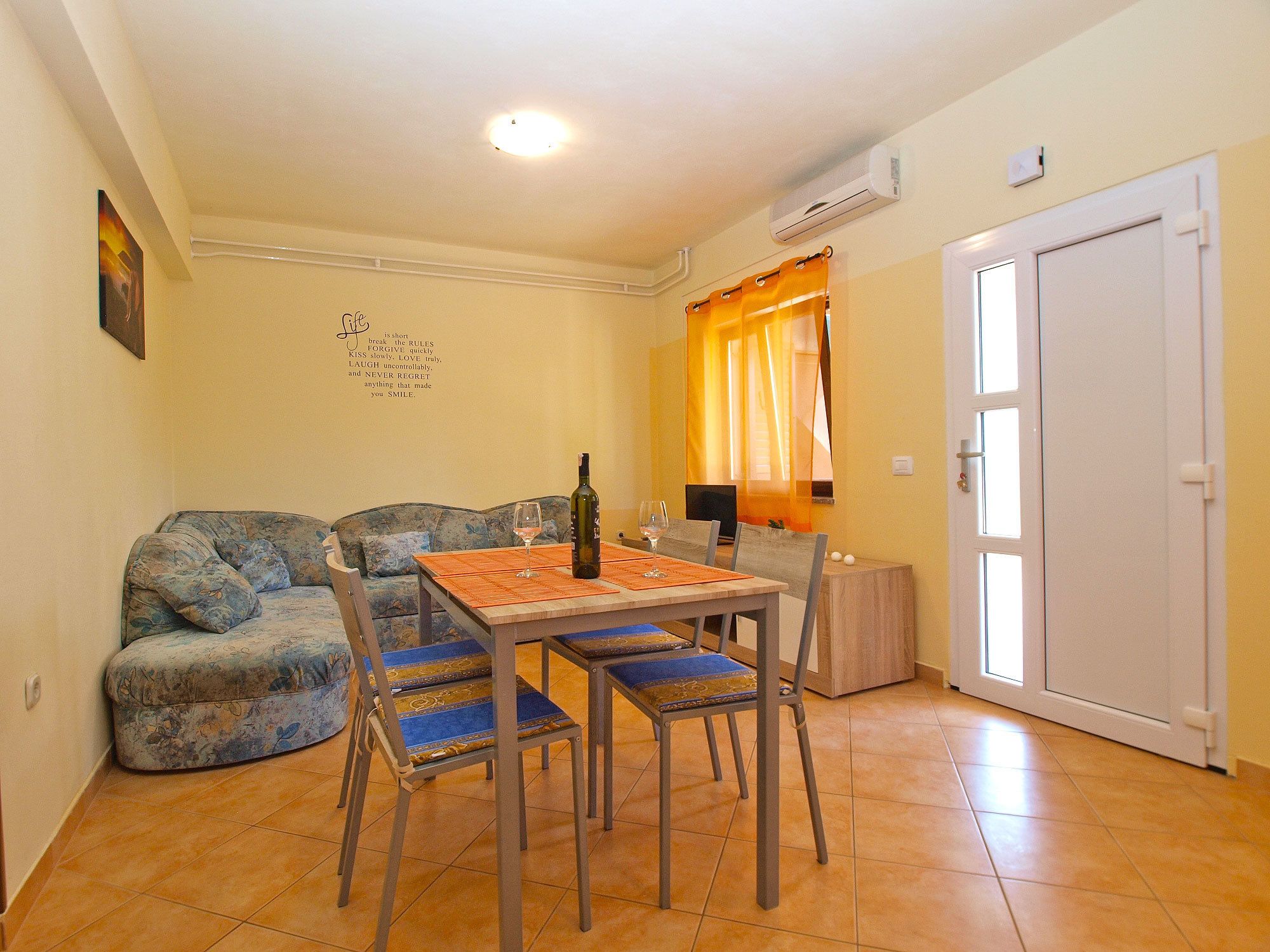 A cozy living room with a sofa, a dining table with chairs, a bottle of wine, and a decorative wall piece.