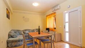 A cozy living room with a sofa, a dining table with chairs, a bottle of wine, and a decorative wall piece. - Apartment 1468 (Fazana)