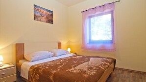 A bedroom with a bed, a nightstand, a lamp, a window with a curtain, and a painting on the wall. - Apartment 1468 (Fazana)