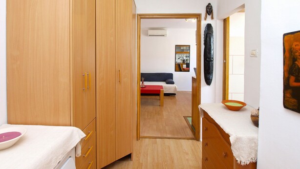 Una habitación con un armario de madera, un sofá rojo, una mesa blanca con un cuenco y una escultura en la pared.