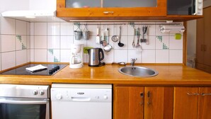 Una cocina con armarios de madera, un lavamanos de acero inoxidable, una cafetera y diversos utensilios colgados en la pared.