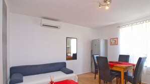 Un espacio habitable compacto con sofá, una mesa de comedor con sillas, refrigerador y aire acondicionado.