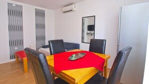 Un comedor con una mesa de madera, sillas negras y un mantel rojo. Hay un espejo en la pared y una unidad de aire acondicionado sobre la mesa.