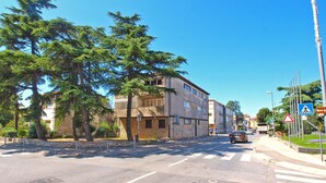 Una intersección de calles con un paso de peatones, un edificio de piedra de varios pisos y un cielo azul despejado.