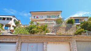 A multi-story building with a stone facade, a balcony with railings, and a yellow trash bin. - Apartment 1471 (Labin)