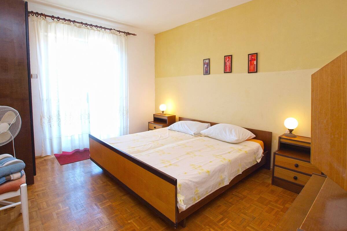 Une chambre à coucher avec un lit en bois, deux tables de chevet avec des lampes, une chaise et une fenêtre avec des rideaux.