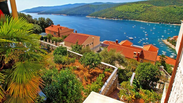 A coastal town with terracotta-roofed buildings, a marina with boats, and lush greenery. - Apartment 1471 (Labin)