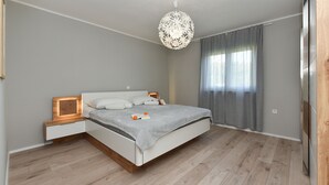 Un dormitorio con cama, mesitas de noche, lámpara colgante y ventana con cortinas.