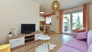 Una sala moderna con televisor de pantalla plana, una mesa redonda blanca, un sofá y un comedor con mesa y sillas.