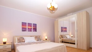 Una camera da letto con un letto grande, comodini con lampade, un armadio e tre dipinti raffiguranti un tramonto alle pareti.