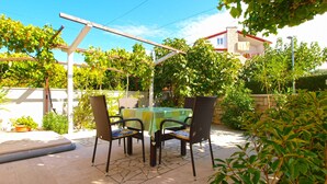 Patio esterno con tavolo e sedie, immerso nel verde e riparato da una pergola.