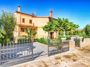 A two-story building with a tiled roof, a gated entrance, and a garden with trees and shrubs. - Apartment 1482 (Medulin)