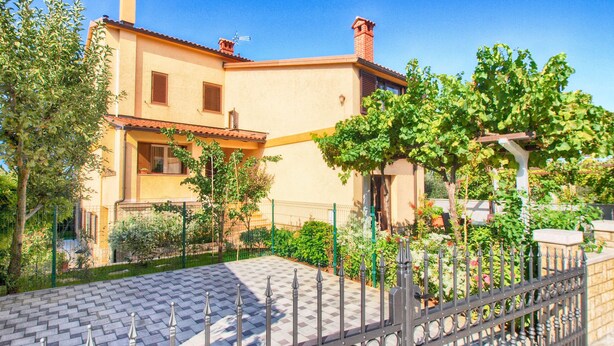 Una casa a due piani con un patio piastrellato e un recinto in metallo.