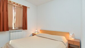 Un dormitorio con cama, mesitas de noche, un radiador y una ventana con cortinas.