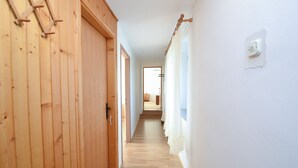A hallway with wooden walls and a wooden floor, leading to a room with a bed and a window. - Apartment 1492 (Barban)