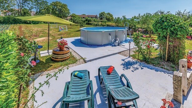 An outdoor swimming pool area with a covered patio, lounge chairs, and a garden with potted plants. - Apartment 1492 (Barban)
