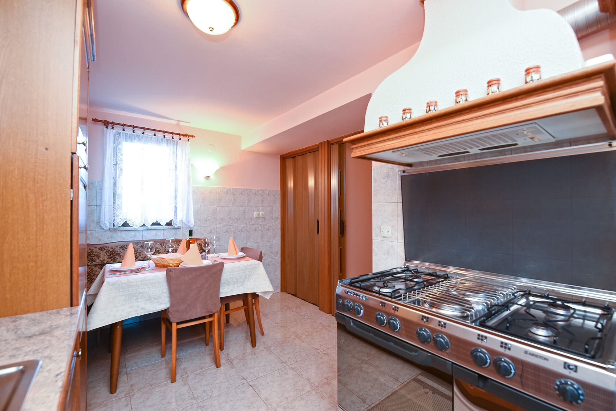A compact kitchen with a gas stove, a dining table with chairs, and a window with curtains.