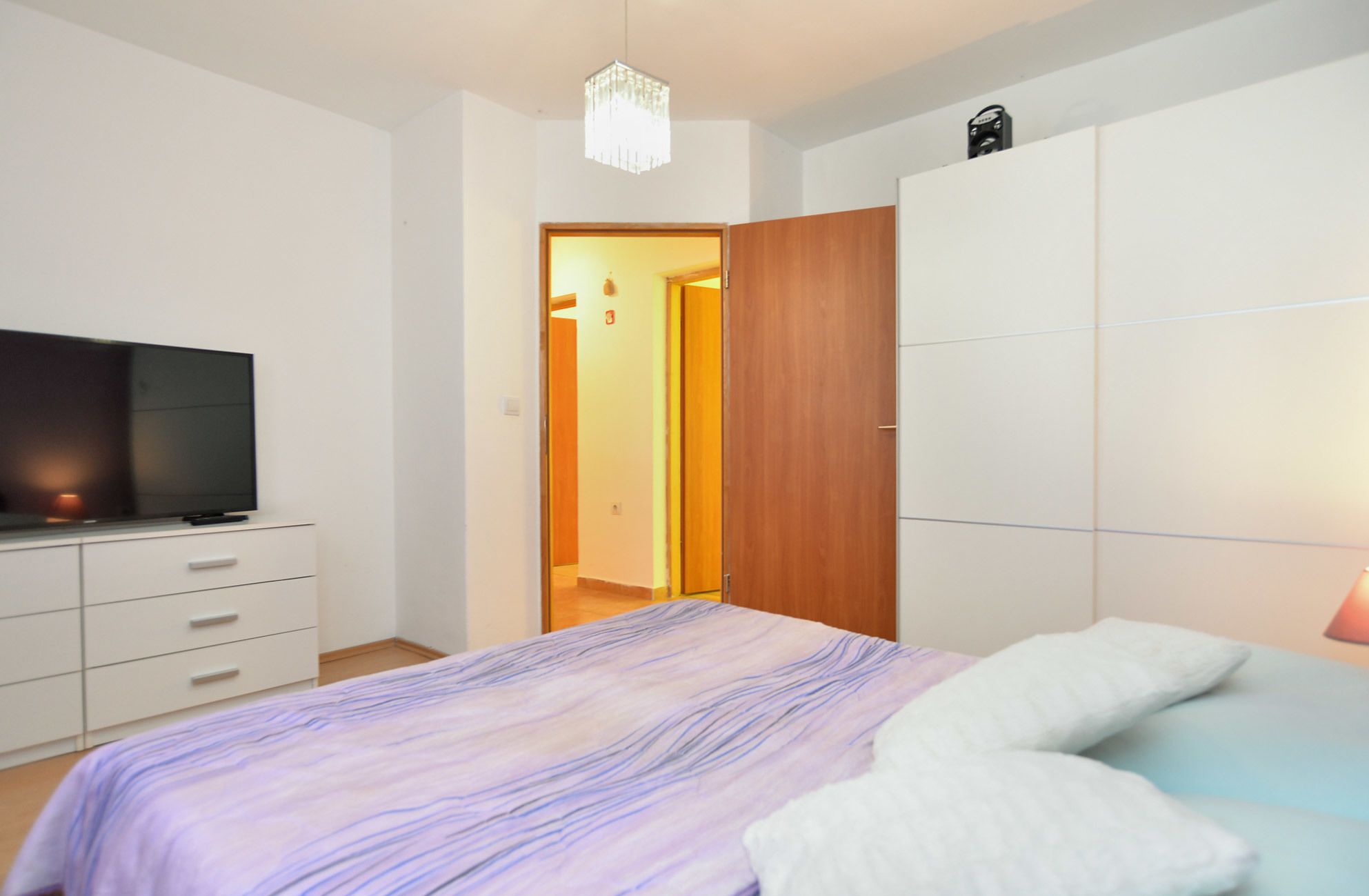 Ein Schlafzimmer mit einem Bett, einem Fernseher, einem Kleiderschrank und einer Tür zu einem anderen Raum.
