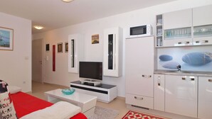 A modern, well-lit living room with a flat-screen TV, a red sofa, and a kitchen area with white cabinets and a microwave. - Apartment 1507 (Fazana)