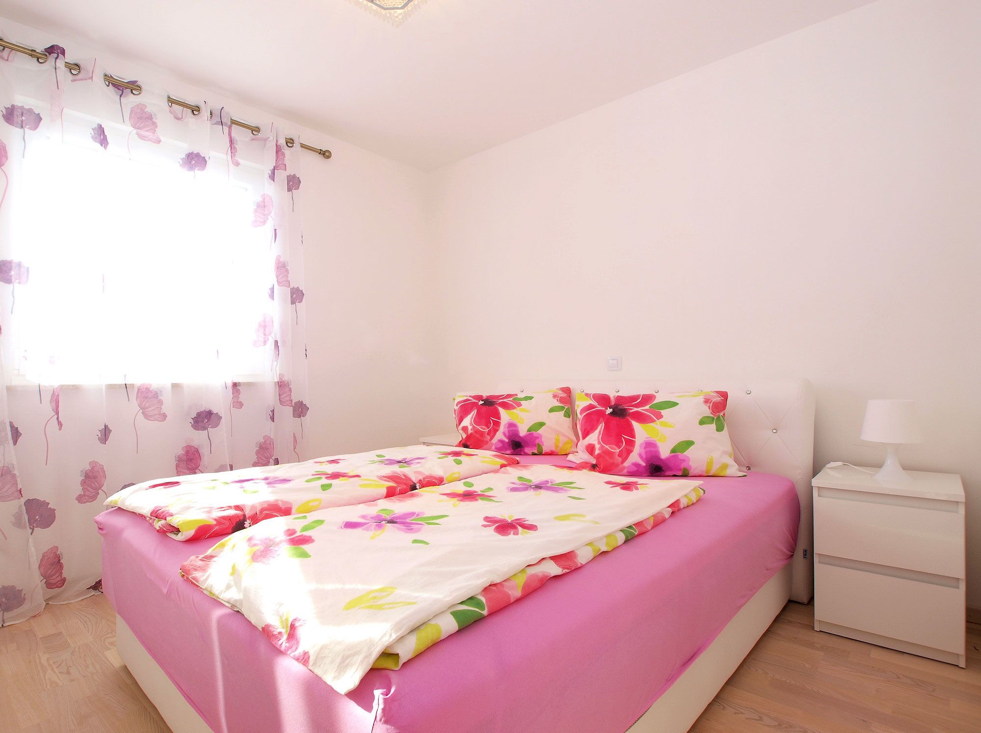 A bedroom with a bed, a nightstand, and a window with floral curtains.