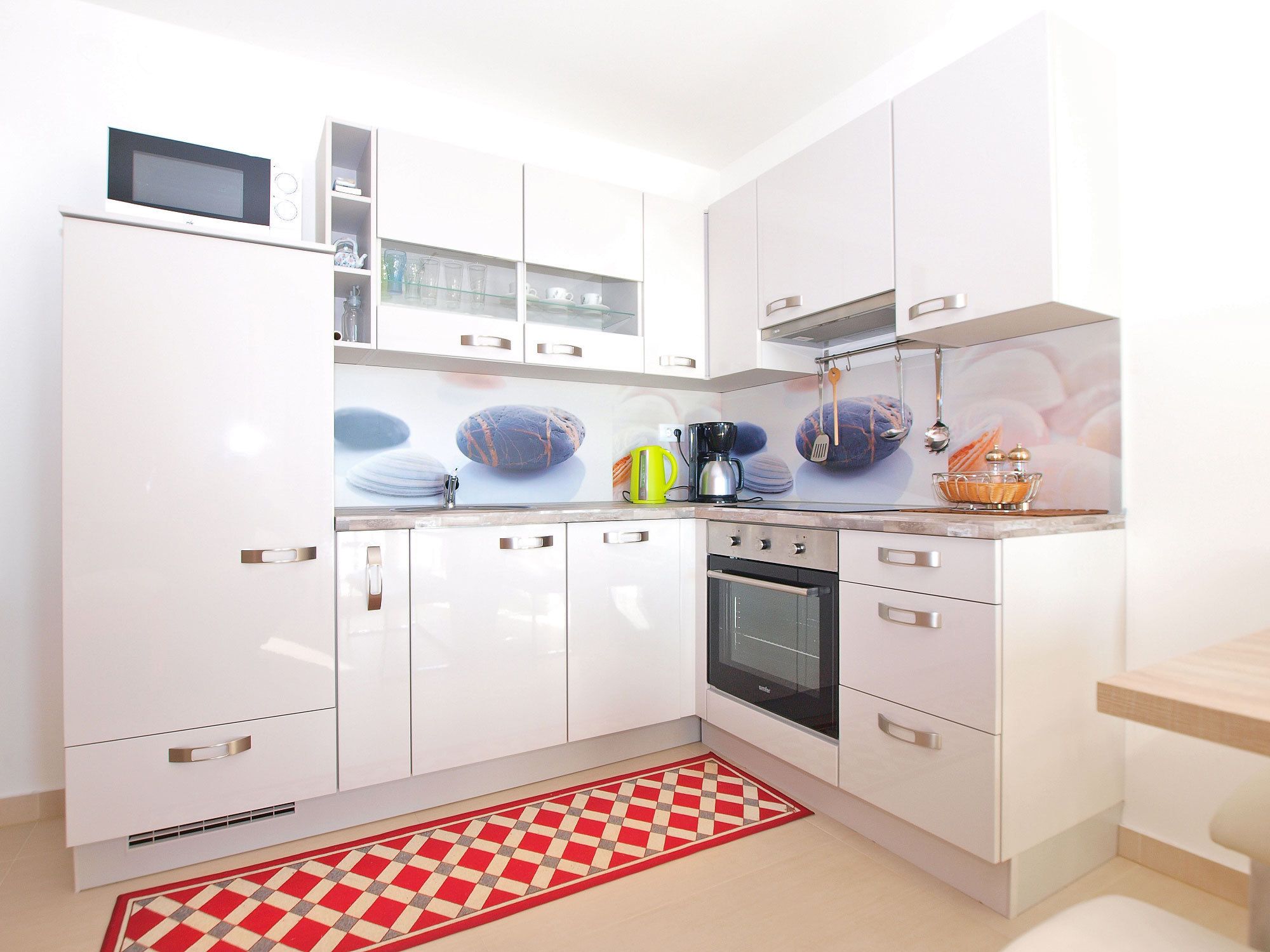 Una cocina moderna con armarios blancos, un microondas, una cafetera y un tapete a cuadros.