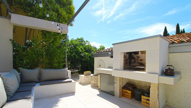 An outdoor patio with a built-in barbecue area, a seating area with cushions, and a tiled floor. - House 1529 (Medulin)