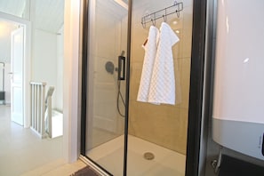 Et bruseområde med glasvægge, et kontrolpanel, en håndklæderække med to håndklæder samt en hvid vask med hane.