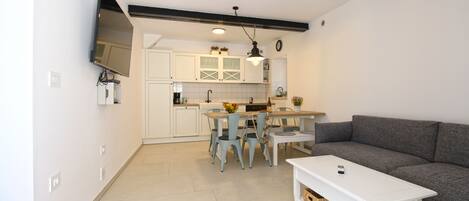 Un espacio habitable compacto con kitchenette, un comedor con sillas variadas y un sofá gris.